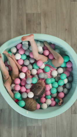 toddler boy and preschooler girl play together happily lying in turquoise dry pool with plastic balls. satisfied children relax in cozy living room