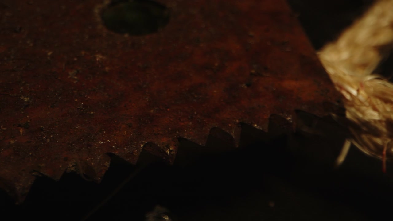 Horrorkoncept: Detaljeret makro-kamerakørsel af en rusten og beskidt sav og blodige reb.