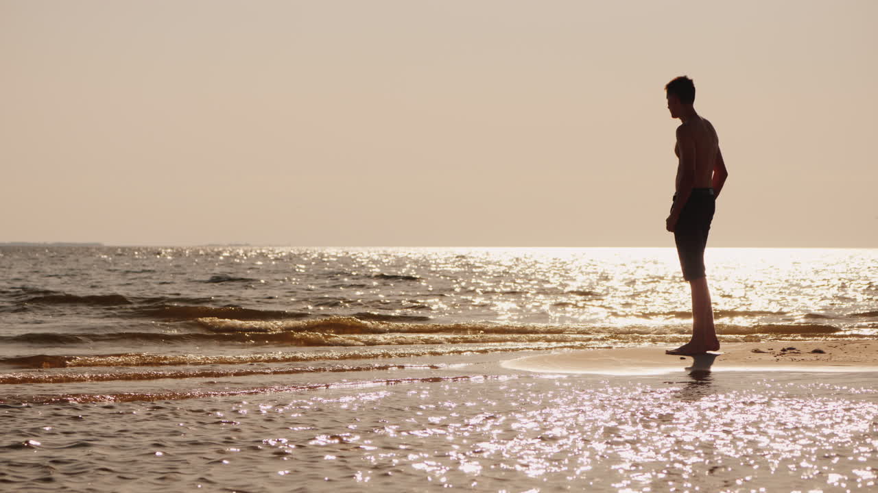 태양의 섬광을 바라보며 작은 모래섬에 서 있는 젊은 독신 남자의 실루엣