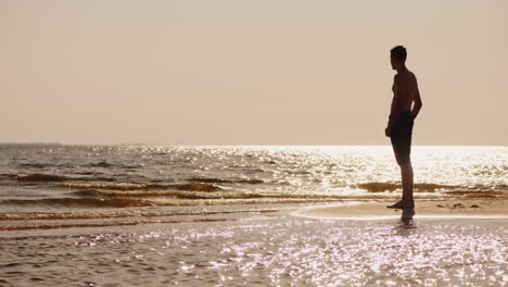 Silhouette-Eines-Jungen-Alleinstehenden-Mannes,-Der-Auf-Einer-Kleinen-Sandinsel-Steht-und-In-Den-Glanz-Der-Sonne-Schaut