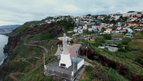 Aerial-view-orbiting-giant-Cristo-Rei-religious-sightseeing-sculpture-on-Ponta-Garajau-lush-coastal-hillside