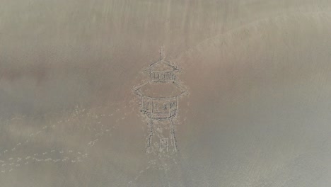 aerial, rising, drone shot, top down above a drawing of a water tower in sand, at a beach, in langeoog, germany