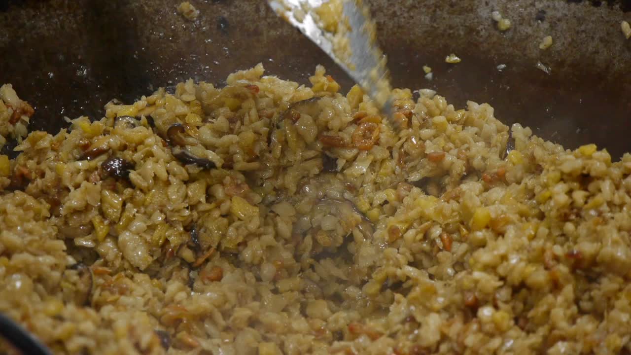 Primer plano de arroz frito asiático tradicional siendo salteado y removido con una espátula en un wok.