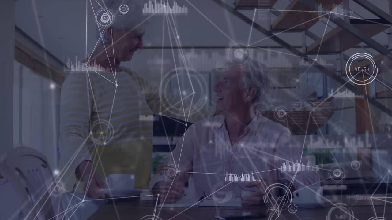 Senior man writing document initiating data charts overlay, woman placing coffee fueling tech work