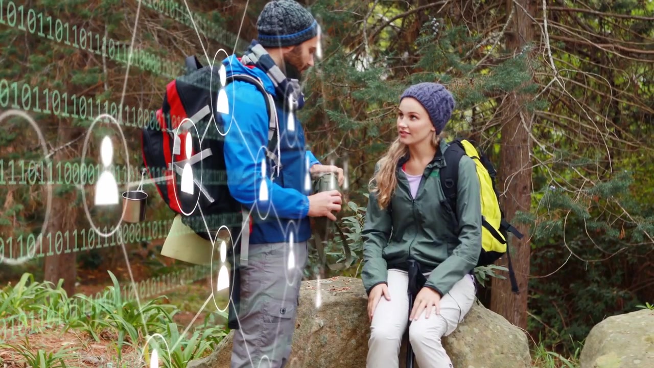 Wanderndes Paar, Mann hält inne, holt Flasche und gießt wärmendes Getränk ein, während sie den Wald mit einer binären Technologie-Überlagerung aufnimmt.