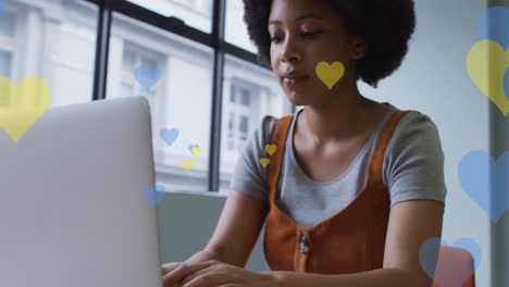 Animation-of-hearts-falling-over-african-american-woman-using-laptop