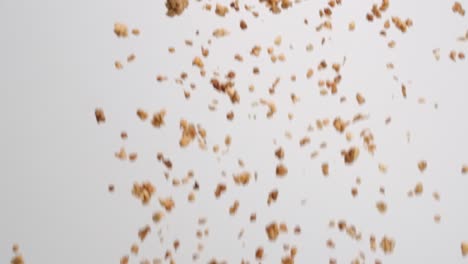 racimos de granola marrón crujiente lloviendo sobre fondo blanco en cámara lenta