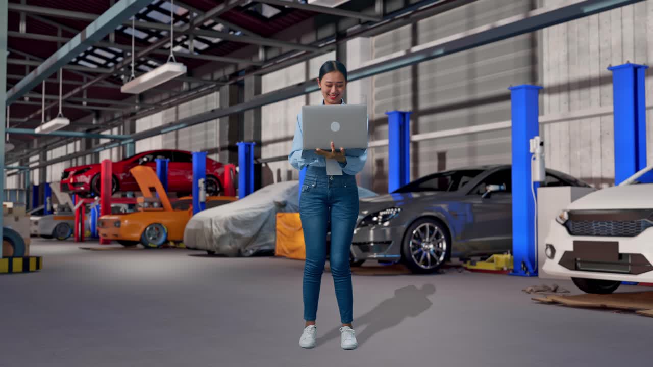 Corpo inteiro de uma mulher asiática com o laptop dela em uma oficina de conserto de automóveis. Ela observa olhando ao redor antes de se concentrar no laptop.