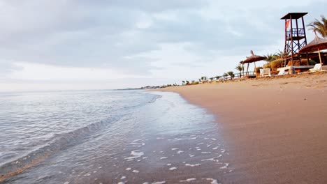 Playa-De-Arena-Tropical-Con-Sombrillas-Y-Tumbonas-En-La-Costa-De-Chipre,-Vista-En-Movimiento