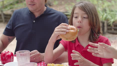 close-up of happy boy eating burger during a picnic in the forest with his family