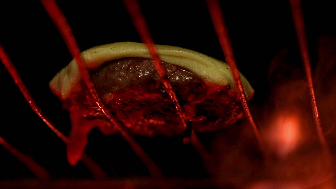 Beef hamburger on the top of a grill over the fire with a slice of cheese on top, close up view macro shot.