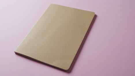 Close-up-of-closed-brown-book-with-copy-space-on-pink-background-in-slow-motion