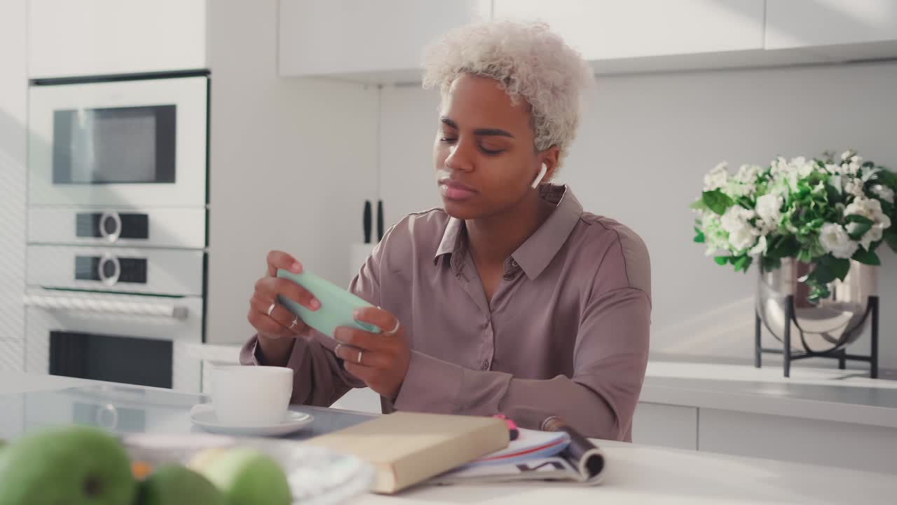 Young gamer african american woman plays games on mobile phone during breakfast