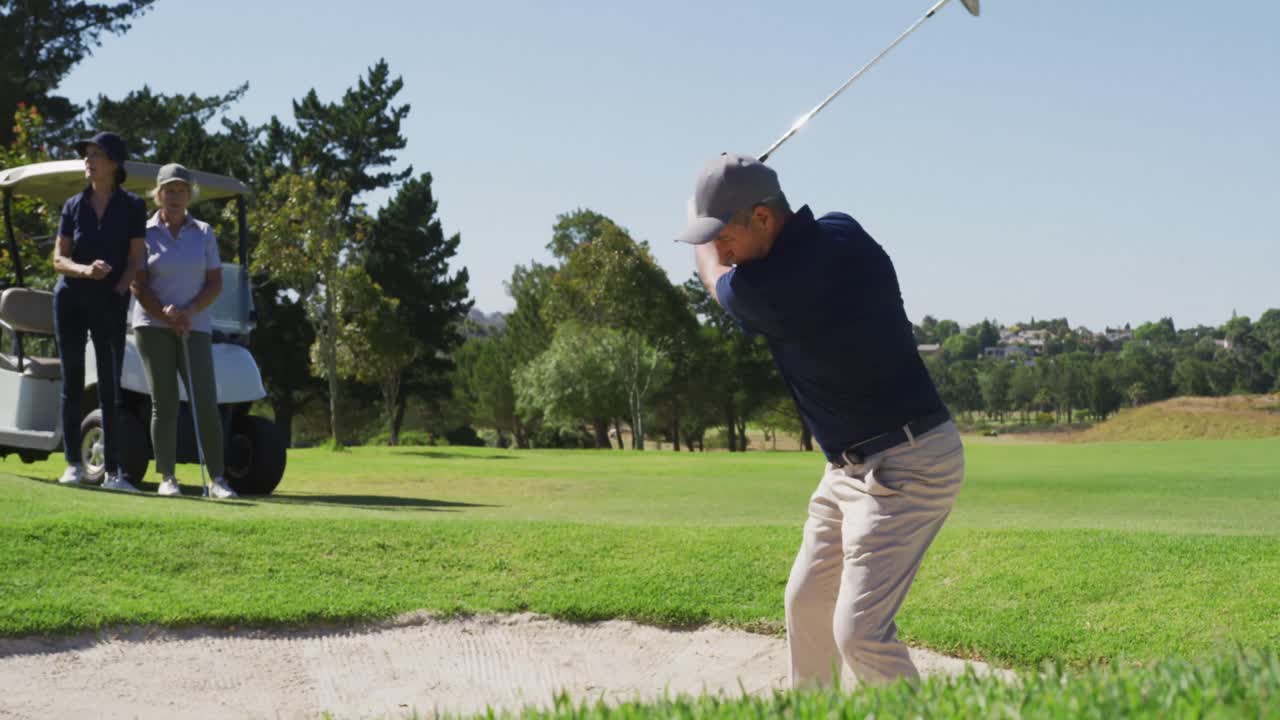 밝은  ⁇ 은 날에 골프 코스에서 모래 함정에서 골프 공을 때리는 백인 노인