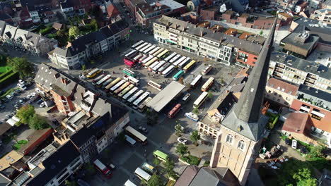 an aerial shot of busses gathering on a town square with the church dominating the view