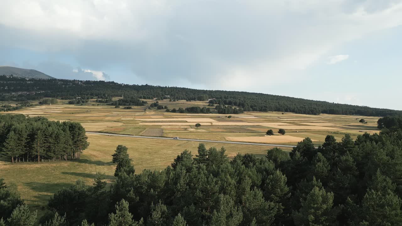 Lone car is driving along a country road in the south of france, near the village of les angles. The car is passing through a valley with pine forests and fields