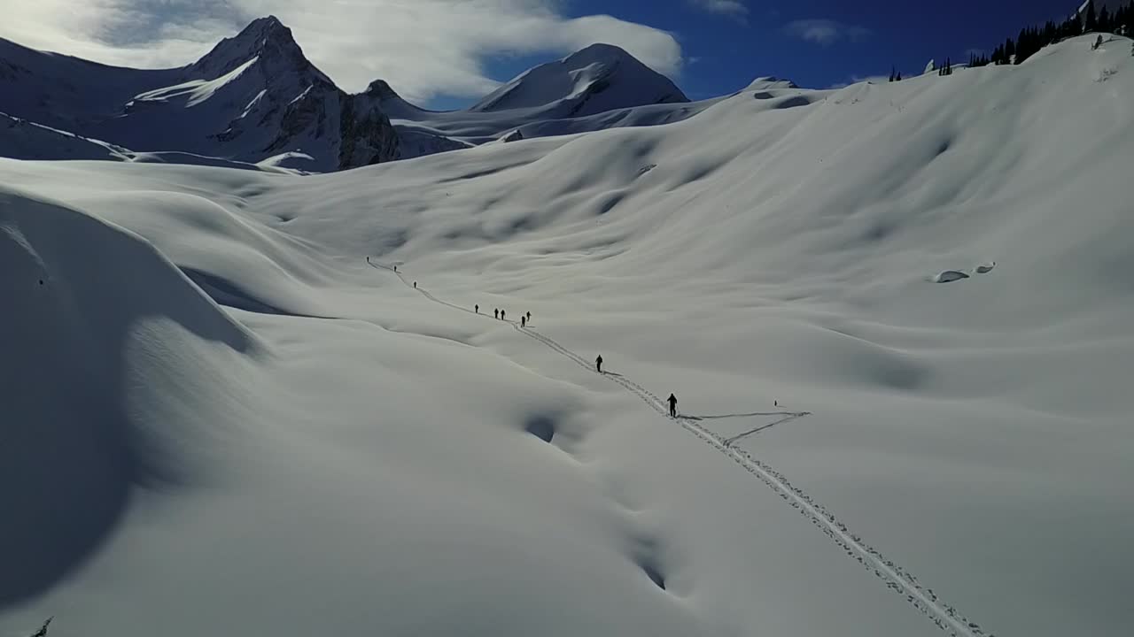 백컨트리 스키어들이 산을 향해 오르는 동안 스킨트랙 위를 비행하는 드론