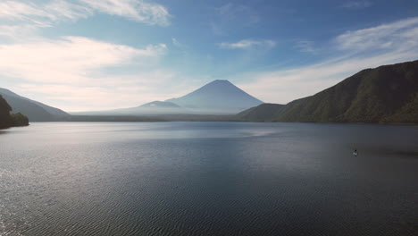 Morning-serenity-Mount-Fuji-gracefully-emerges-through-the-tranquil-woods,-enchanting-the-shores-of-Lake-Motosu-with-its-majestic-presence