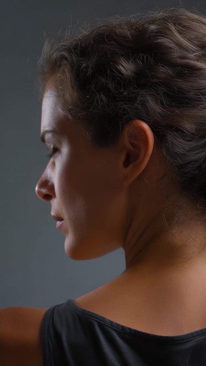 Un Momento Contemplativo Catturato di Profilo, che Evidenzia l'Espressione Serena e i Capelli Texturizzati di una Giovane Donna su uno Sfondo Grigio Tenue, Evocando Introspezione