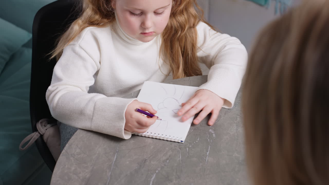 Focused girl drawing with purple pencil in notebook at table, concentrating on sketch, childhood creativity, learning, artistic development, education, imagination, study and artistic expression