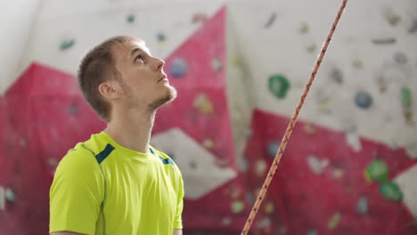 portrait of beautiful man rock climber belaying another climber with rope. indoors artificial climbing wall and equipment.