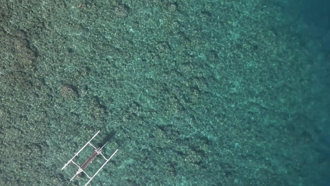 Flyover overview of trimaran canoe in clear shallow sea water of Bali