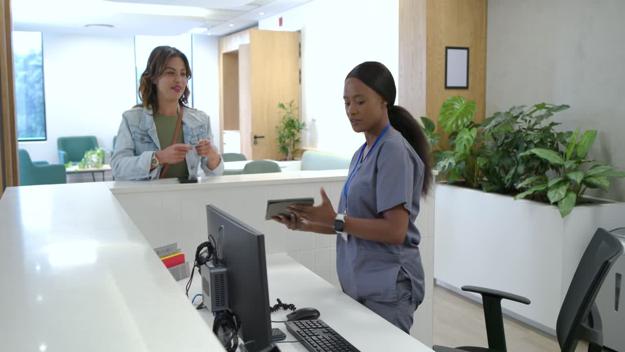 Receptionist in divisa medica controlla il tablet dopo che una donna mostra il telefono al banco della clinica durante il check-in