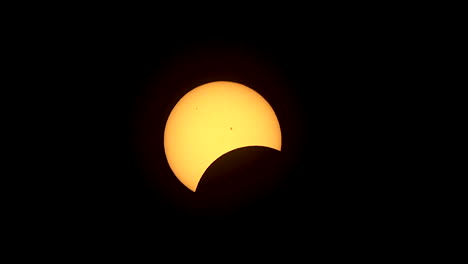 zoom-out of partially eclipsed sun with two sunspots visible on the face of the sun