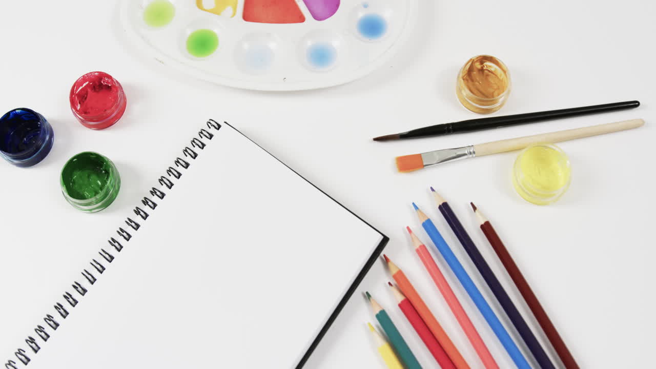 primer plano de pinturas, cuadernos y pinceles con espacio para copiar sobre un fondo blanco