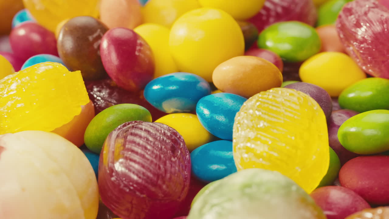 Colorful dragee candies, lollipops, bonbons on white background, move in circle, side view close-up. Summer bright texture studio shot for store, supermarket. Mix of children's sweets made of sugar.