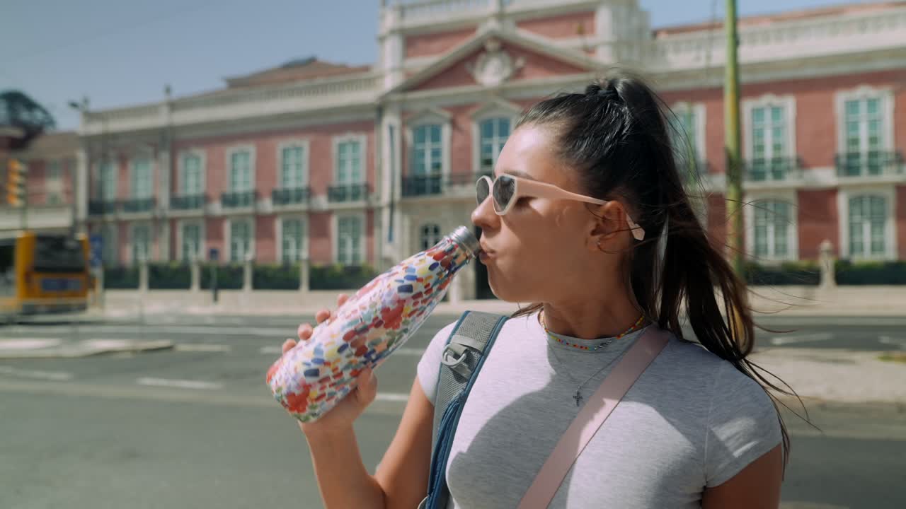 Giovane donna che beve acqua da una bottiglia per strada in città