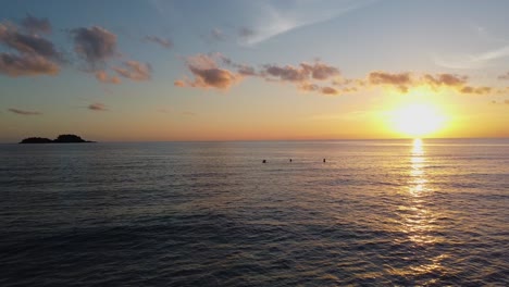 aéreo: el dron viaja bajo sobre las tranquilas aguas costeras, la gente nada al atardecer con islas en el fondo