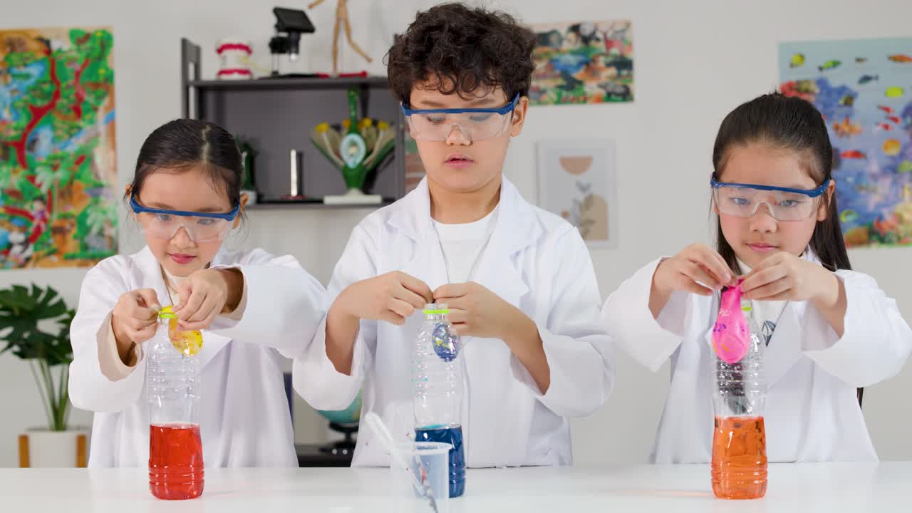 Three young students perform a chemical reaction experiment using plastic bottles and colorful balloons