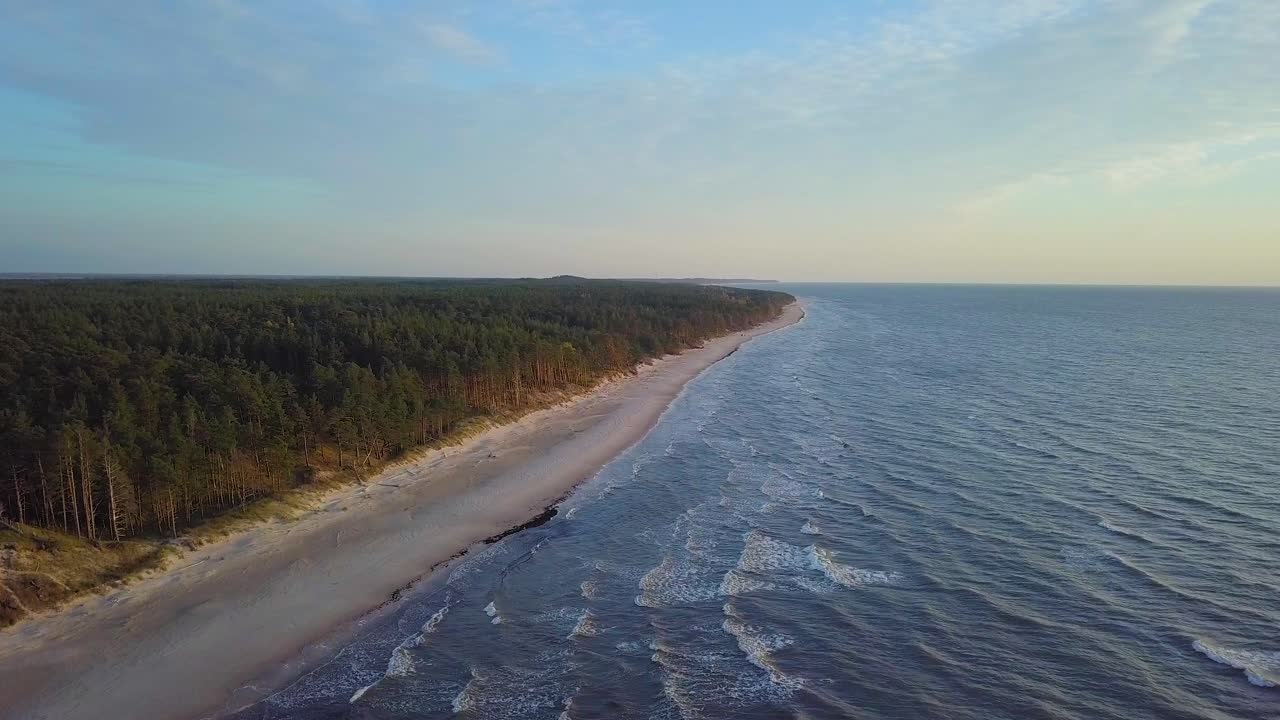Vacker flygvy över Östersjökusten en solig kväll, solnedgång, gyllene timmen, strand med vit sand, kusterosion, klimatförändringar, vidvinkeldrönarbild som rör sig framåt