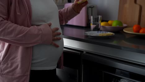 pregnant woman drinking water and eating a healthy snack in the kitchen