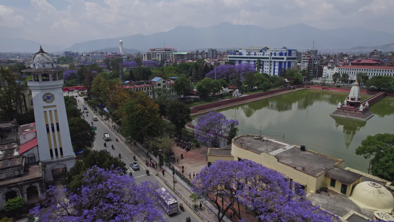 A beautiful drone view of Kathmandu Valley featuring Rani Pokhari, Ghantaghar, and blooming Jacaranda flowers. This aerial shot highlights the valley’s culture, colors, heritage, and timeless urban