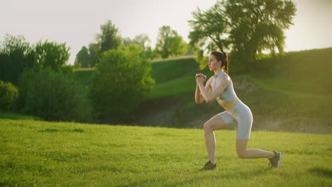 a woman performs squats on one leg with a backward lunge and a high hip lift. training in the park in summer for legs and thighs at sunset