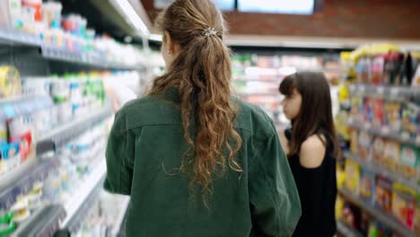 Teen-girl-and-her-mom-or-sister-shopping-in-the-supermarket-with-cart,-rear-view