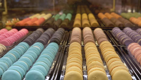 rows of multicoloured macaroons set out on display, mirrored reflection in background as shot pan's across