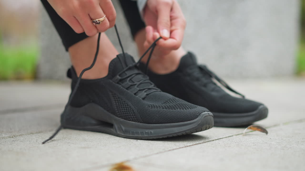 Close-up shot of sport girl tightening black shoelace on running shoes, preparing for outdoor fitness training, focused on footwear and sports readiness before workout session