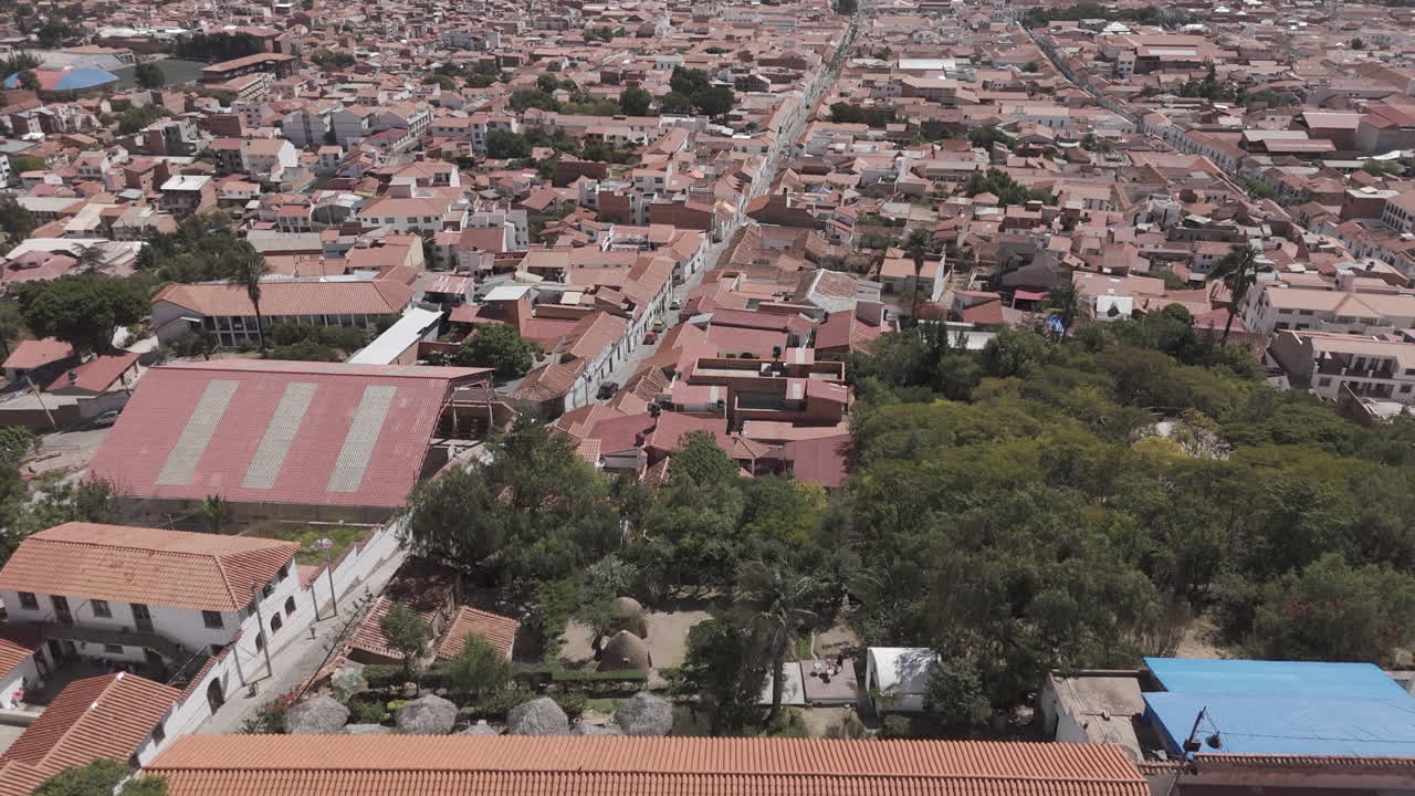 Wide drone shot of Sucre Bolivia on a bright day with blue sky starting over the square on top of the city LOG