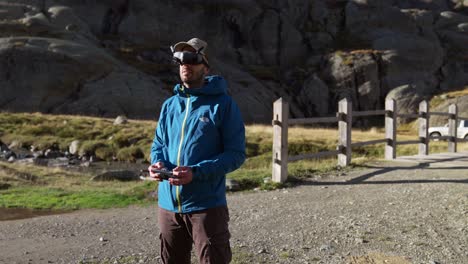 man wearing virtual reality goggles to operate drone outdoors in the mountains