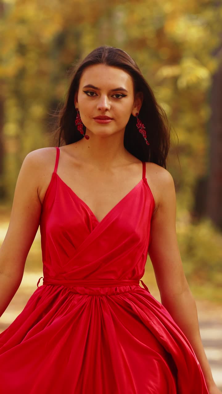 Donna elegante in abito rosso incanta con movimenti aggraziati sullo sfondo di una lussureggiante foresta autunnale, esibendo la bellezza e i colori della natura in perfetta armonia.