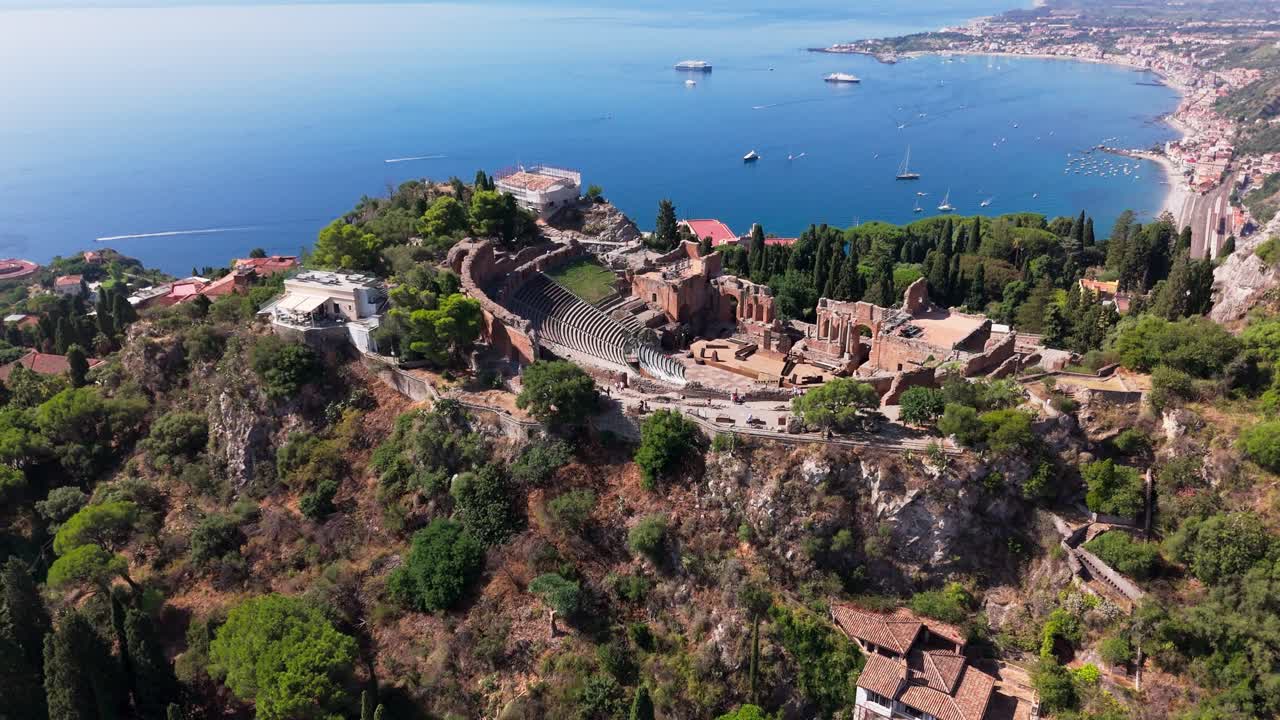 Drone lifts up and pans down over Taormina Amphitheatre, highlighting its structure with surrounding town and coastline views