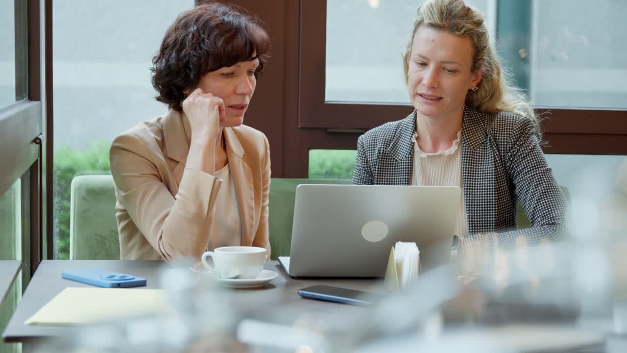 Two female colleagues discussing business matters during a meeting in a cafe. The professional women are working together on a laptop