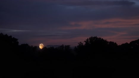 Funkelndes-Gelbes-Feuerwerk-Explodiert-In-Der-Ferne-Mit-Rotem,-Dunstigem-Violettem-Glühen,-Zeitlupe