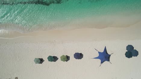 turquoise waters meeting white sandy beach with colorful umbrellas, aerial view