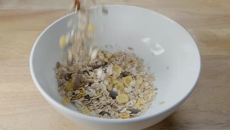 slow motion slider shot of pouring muesli into a white cereal bowl on a kitchen counter for breakfast