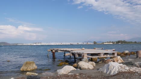 Serene Seascape: Wooden Pier on Rocky Shore with Boats in Background