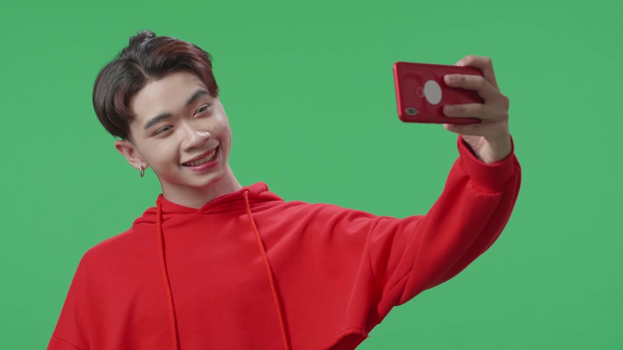 The Smiling Asian Transgender Male Making Selfie While Standing On Green Screen In The Studio